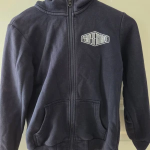 Mörkblå hoodie från Peak Performance - Snygg mörkblå hoodie från Peak Performance med dragkedja och huva. Tröjan har två fickor framtill och logga på bröstet. Perfekt för chill dagar och har en klassisk look som funkar till det mesta.