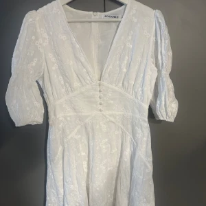 Vit blommig kortklänning från Adoore - Finaste vita kortklänningen från Adoore med broderade blommor, puffiga korta ärmar och djup v-ringning. Den har en markerad midja, så klänningen passar även en i strl 38 eftersom de Adoore är lite mindre i strl. Endast använd 1 gång på min student! Köptes för 1495 kr och säljs inte längre i exakt denna modell.