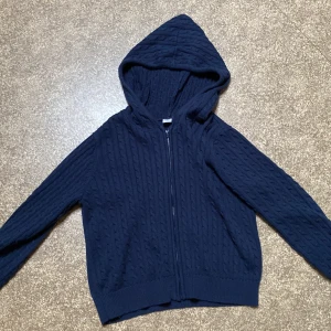 Mörkblå stickad hoodie från Lindex - Mörkblå stickad hoodie från Lindex med dragkedja framtill och huva. Tröjan har ett snyggt kabelstickat mönster och långa ärmar. Använd några gånger men är som ny. 