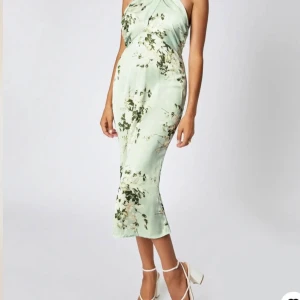 Mintgrön blommig halterneckklänning - Superfin mintgrön halterneckklänning med blommigt mönster och figurnära passform. Klänningen är axelbandslös med knyt i nacken går även att knyta i kors framtill eller rakt över. Passar M. Aldrig andvänd med prislappen på