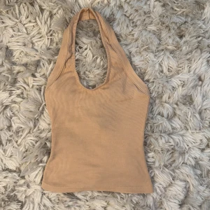 Beige ribbad halterneck topp Boohoo - Säljer en beige ribbad halterneck topp från Boohoo i storlek 36. Toppen är ärmlös med djup urringning och smickrande passform. Perfekt till jeans eller kjol för en trendig look. Aldrig använd