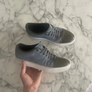 Gråblå sneakers från Lanvin  - Snygga sneakers från Lanvin i gråblå mocka i storlek ca 40 men sitter som 42 gör, lackad grå tå och vita sulor. Skorna har snörning och detaljer i skinn på plösen och insidan. Perfekta för dig som vill ha en stilren men unik sneaker med exklusiv känsla.