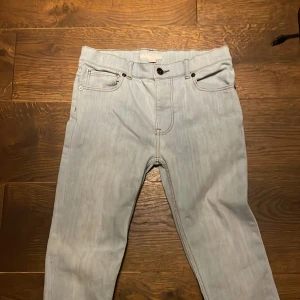 Ljusblå jeans från Burberry - Säljer ett par ljusblå jeans från Burberry med klassisk femficksdesign och raka ben. Jeansen har svarta knappar och detaljer samt diskret Burberry-logga på bakfickan. Tillverkade i mjuk bomull för en bekväm känsla och snygg passform.