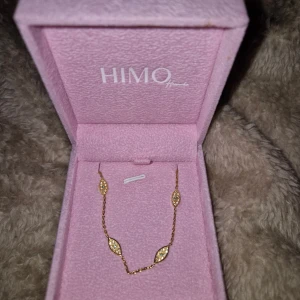 Guldigt halsband med glittriga detaljer - Supersnyggt halsband från HIMO i guldton med fyra bladformade hängen, dekorerade med små glittrande stenar. Kedjan är tunn och elegant, perfekt för att ge din outfit lite extra bling. Kommer i en söt rosa ask. OBS asken ingår inte