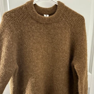 Brun stickad tröja med rund hals - Mysig brun stickad tröja från H&M med rund halsringning och lång ärm. Tröjan har en fluffig och grovstickad känsla som ger en avslappnad och trendig look. Perfekt för lager-på-lager under kyliga dagar.