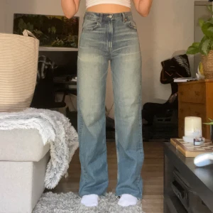 Högmidjade blåa jeans från Zara - högmidjade jeans i ljusblå tvätt med raka ben och snyggt fransad rå kant nertill. Jeansen har fem fickor, knappgylf och tydliga slitningar för en cool vintagekänsla. Perfekta för dig som gillar en avslappnad och tidlös stil.