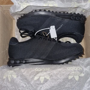 Svarta Adidas LA Trainer sneakers - Snygga helsvarta Adidas LA Trainer sneakers med ovandel i mesh och klassisk snörning. Skorna har en sportig look med diskreta detaljer och en robust sula med gummidubbar för extra grepp. 