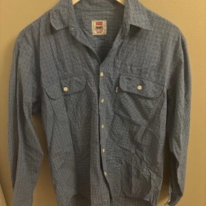 Blårutig skjorta från Levi's, S - Säljer en blå rutig skjorta från Levi's i storlek S. Skjortan har klassisk krage, två bröstfickor med lock och vita knappar framtill. Tillverkad i mjuk bomull och har lång ärm. Perfekt för dig som gillar en avslappnad men ändå stilren look. Vid frågor bara att höra av sig, Mvh Oscar