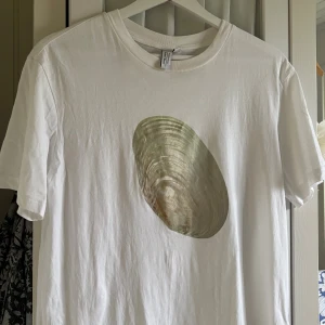 Vit t-shirt med snäckmotiv & Other Stories - Vit t-shirt från & Other Stories med ett stort snäckskal-tryck framtill. Klassisk passform med rund halsringning och korta ärmar. 