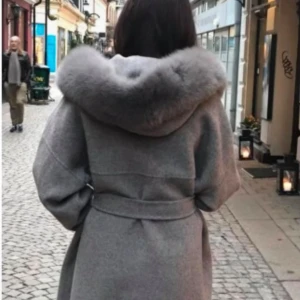 Grå kappa med päls huva - Snygg grå kappa med oversized passform, stor huva med fluffig päls och knytskärp i midjan. Jackan har stora fickor framtill och är perfekt för kalla dagar. Äkta päls och saknas en knapp vid luvan men inget man märker av
