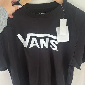 Svart Vans t-shirt med logga XL - Svart t-shirt från Vans i storlek XL med stor vit Vans-logga tryckt på bröstet. Klassisk rund hals och korta ärmar. Tillverkad i mjuk bomull som är skön mot huden. Perfekt för dig som gillar streetwear och enkel stil.