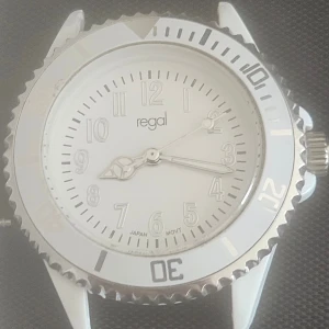 Vit klocka från Regal med två armband - Snygg vit klocka från Regal med rund urtavla och silverfärgade detaljer. Klockan kommer med två utbytbara armband, ett i sportig gummi och ett i länkstil. Perfekt accessoar för dig som gillar stilren och clean design.