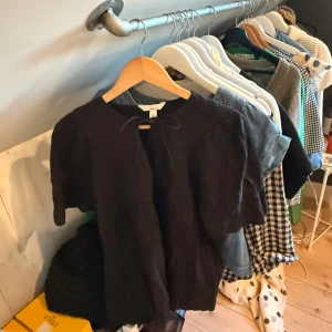 Svart blus med knyt HM - Svart blus från H&M Mama i storlek S. Blusen har korta puffärmar och en rund halsringning med knytband framtill. Tillverkad i ett lätt och luftigt bomullsmaterial, perfekt för en chill och stilren look. Jag har själv använt den bara som en vanlig lite oversized blus trots att den är från Mamaavdelningen