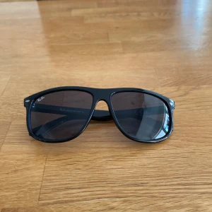 Svarta solbrillor  - Snygga svarta Ray-Ban solglasögon med klassisk form och mörka glas. Ramen är i blank plast. Perfekta för soliga dagar.