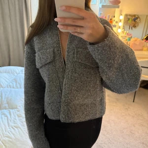 Grå ulljacka med dragkedja - Säljer en snygg grå jacka i ull med croppad passform och dragkedja framtill från Zara. Jackan har två stora bröstfickor och långa ärmar. Aldrig använd