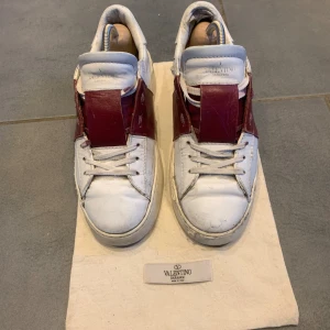 Valentino Garavani Open sneakers vit/röd - Snygga Valentino Garavani Open sneakers i vitt skinn med bred vinröd. Vänstern skon är limmad på toppen av skon men annars är allt bra med skorna. Påsen kommer med och om ni vill ha fler bilder bara skriv. Skorna är i st 41.