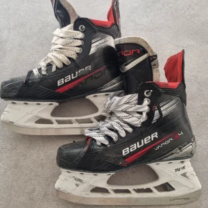 Bauer Vapor X4 hockeyskridskor - Säljer ett par Bauer Vapor X4 hockeyskridskor i svart med röda och vita detaljer. Skridskorna har vit plastskena, kraftig snörning och en sportig design. Perfekta för dig som vill ha grym kontroll på isen. Snygg och modern look med klassisk Bauer-känsla. Storlek 6, fit 3.
