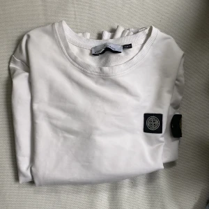 Vit Stone Island sweatshirt - Vit långärmad sweatshirt från Stone Island i slim fit-modell. Tröjan har klassisk rund hals, ribbade muddar och den ikoniska Stone Island-loggan på ärmen. Tillverkad i mjuk bomull som känns skön mot huden. Perfekt för dig som gillar stilrena och snygga plagg. Storleken är L slim fit men sitter mer som en M. Väldigt bra skick. PRIS KAN DISKUTERAS 
