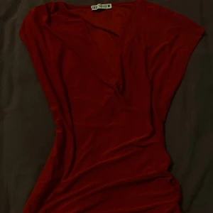 Röd blus från Zara - Snygg röd omlottklänning från Zara i storlek S. Klänningen har korta ärmar och v-ringning, vilket ger en stilren och trendig look. Perfekt för dig som gillar en enkel men elegant stil.