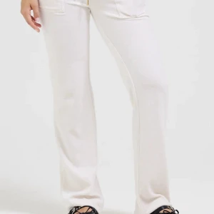 Vita mjukisbyxor Juicy Couture XS - Supermjuka vita mjukisbyxor från Juicy Couture med dragsko i midjan och stora fickor fram och bak. Byxorna har en relaxed passform med raka ben och är perfekta för en chill och trendig look. Klassisk Juicy-stil i skönt material.