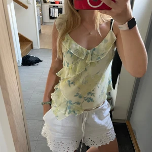 Blommig volangtop Rita Ora x Primark S - Supersöt blommig linnetopp från Rita Ora x Primark i storlek S. Toppen är ljusgul med blå och gröna blommor, har volangdetaljer framtill och smala knytbara axelband. Luftigt material, perfekt för varma dagar och somriga vibes.