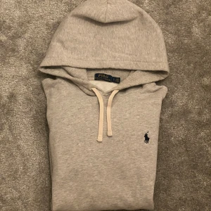 Grå hoodie från Polo Ralph Lauren - Snygg grå hoodie från Polo Ralph Lauren med klassisk broderad logga på bröstet. Tröjan är nästan helt ny och har tvättats max 3 gånger.