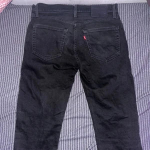 Levi's 511 svarta jeans W32 L32 - Svarta Levi's 511 jeans med klassisk femficksdesign och smal passform. Jeansen har dragkedjegylf, bälteshällor och den ikoniska röda Levi's-taggen på bakfickan. Tillverkade i slitstarkt jeanstyg som ger en snygg och stilren look.