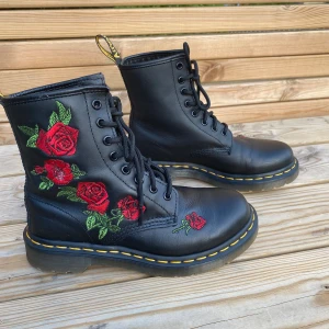 Dr. Martens 1460 Vonda boots med rosor - Svarta Dr. Martens 1460 Vonda boots i skinn med broderade röda rosor på sidan. Klassisk gul söm runt sulan, snörning framtill och robust platt sula. Endast använda 3 gånger och är i mycket bra skick. 