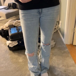 Ljusblå ripped jeans från Nelly - Säljer ett par ljusblå jeans från Nelly med slitna knän och raka ben. Jeansen har coola orange broderade detaljer på bakfickorna och klassisk femficksdesign. Perfekt för dig som gillar en avslappnad och trendig look.