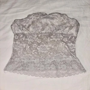 Vit spets tubtopp med volangkant - Säljer en söt vit tubtopp i spets med blommigt mönster och volangkant nertill. Toppen är axelbandslös och har en stretchig insida.