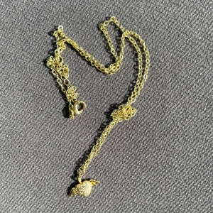 Guldigt halsband med hjärthänge - Snyggt halsband i guldfärgad metall med ett hjärthänge som har små vingar och glittrande stenar på framsidan. Kedjan är tunn och smidig, perfekt för att ge din outfit lite extra bling. Hjärtat har en cool detalj med vingar som gör det unikt.