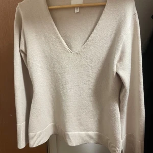 Beige stickad v-ringad tröja H&M - Snygg beige stickad tröja från H&M med djup v-ringning och långa ärmar. Tröjan har ribbade muddar vid ärmslut och nederkant, vilket ger en stilren och modern look. Perfekt att matcha med jeans eller kjol för en chill vibe.