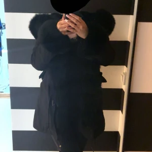 Svart pälsjacka med stor fluffig huva - Säljer en svart pälsjacka med extra stor och fluffig huva. Jackan har en loose passform och är helsvart med mjukt pälsmaterial både på utsidan och insidan. Perfekt för dig som vill ha en riktigt mysig och varm look under kalla dagar.