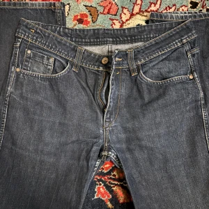 Dylan Raw Denim jeans i mörkblå denim - Snygga jeans från Dylan Raw Denim i mörkblå tvätt med klassisk femficksdesign och kontrastsömmar. Jeansen har raka ben och normal passform, tillverkade i slitstarkt denimtyg. Perfekta för dig som gillar en tidlös och clean look.