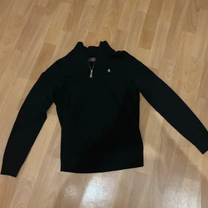 Svart merinoullströja från Morris - Svart långärmad tröja från Morris i 100% merinoull. Tröjan har en stilren design med half zip-dragkedja och liten broderad logga på bröstet. Perfekt för dig som gillar klassisk och clean stil. Köpt för 1900kr på NK.