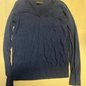 Mörkblå stickad tröja från Stockh LM - Mörkblå stickad tröja från Stockh LM med v-ringad hals och långa ärmar. Den är lite nopprig. Tröjan har en klassisk passform och är tillverkad i mjukt material som passar perfekt för kyligare dagar. Enkel och stilren design som funkar till det mesta.