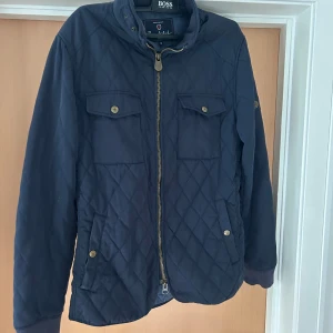 Mörkblå quiltad jacka från Bondelid - Quiltad mörkblå jacka från Bondelid med dragkedja, två bröstfickor med knappar och två sidfickor. Jackan har ståkrage och ribbade muddar vid ärmslut. Perfekt för dig som gillar klassisk och stilren look.