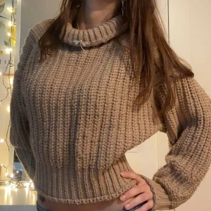 Beige stickad polotröja med ribbad struktur - Supermysig beige stickad polotröja med bred ribbad struktur och lös passform. Tröjan har en hög, rullad polokrage och långa ärmar med extra vidd. Storlek S.