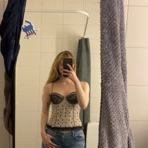  korsettopp med spetsdetaljer - Supersnygg korsettopp med mönster i svart och vitt. Toppen har svarta spetsdetaljer vid bysten och längs nederkanten, samt tunna axelband och liten rosett framtill. 