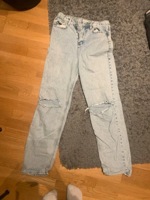 Ljusblå baggy jeans med slitna knän - Säljer ett par ljusblå baggy jeans med raka ben och slitna detaljer över båda knäna. Jeansen har klassisk femficksdesign och är tillverkade i bomull. Perfekta för en avslappnad och trendig look.Andvänt max 5 ggr men för några år sedan!🥰