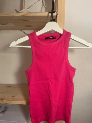 Rosa ribbad linnetopp från Gina Tricot - Snygg rosa ribbad linnetopp från Gina Tricot. Toppen är ärmlös med rund halsringning och har en tight passform. Perfekt att styla med jeans eller kjol för en trendig look.