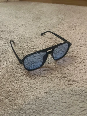 Svarta solglasögon med blåtonade glas - Helt nya och oanvända solglasögon med svart båge och blå-tonat glas. Skriv privat för mer information 