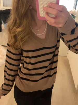 Beige stickad mango tröja med svarta ränder - Säljer en beige stickad tröja med svarta horisontella ränder. Tröjan har v-ringning och långa ärmar. Perfekt för dig som gillar en enkel men snygg stil. Materialet känns mjukt och bekvämt mot huden.