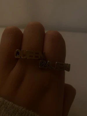 Queen Bajen silverfärgad ring - Unik silverfärgad ring med texten 'QUEEN BAJEN' i stora bokstäver. Ringen är designad för att bäras över två fingrar och har en modern, statement-inspirerad look. Perfekt för dig som vill visa ditt stöd för Bajen på ett stilrent sätt.De kommer från l8H och köpt i butiken! OBS(pris kan diskuteras 