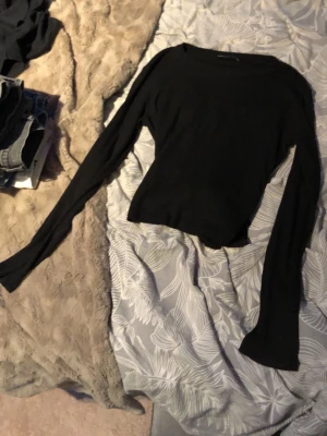 Svart croppad topp med knyt - Snygg svart croppad topp med långa ärmar och knyt i ryggen. Perfekt till höga jeans eller kjol. Tunn och mjuk i materialet, enkel att styla för en trendig look.