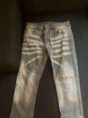 Disquerd Ljusgrå slitna jeans - Säljer ett par ljusgrå  jeans med slitningar framtill. Jeansen har klassisk femficksdesign och är tillverkade i ett mjukt bomullsmaterial med lite stretch. Perfekta för dig som gillar en avslappnad och trendig stil.