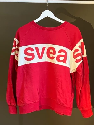 Röd sweatshirt från Svea - Cool röd sweatshirt med bred vit rand och stor logga i rött över bröstet och armarna. Tröjan har rund halsringning, ribbade muddar och avslappnad passform. Perfekt för en sportig och avslappnad stil. Tröjan har även fickor! Köpt från Svea, använt få gånger ❣️
