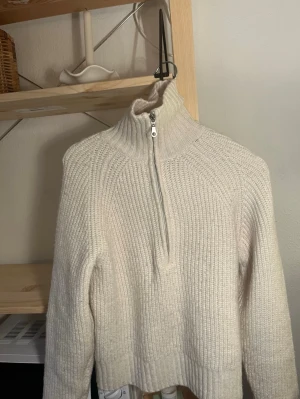 Beige ribbstickad halvzip tröja - Mysig beige stickad tröja med ribbad struktur och halvzip i halsen. Tröjan har hög krage, långa ärmar och avslappnad passform. Perfekt för lager på lager och enkel att styla till olika outfits.