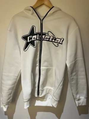 Full zip från Shein - Snygg vit hoodie med dragkedja och svart tryck framtill där det står 'Celestial' med en stor stjärna och planetmotiv. Hoodien har huva, känguruficka och ribbade muddar. Perfekt för en chill och trendig look.