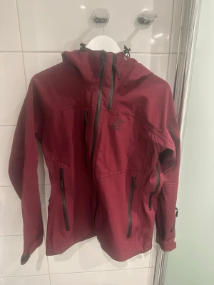 Revolutionrace cyclone 3L shell pro - Snygg vinröd vindjacka från Revolutionrace med huva och flera dragkedjeförsedda fickor. Jackan har lång ärm, justerbar huva och är tillverkad i slitstark polyester. Perfekt för blåsiga dagar och skidåkning. Färgen är helt slutsåld. Tyvärr är jackan lite sliten invändigt vilket syns på bilderna